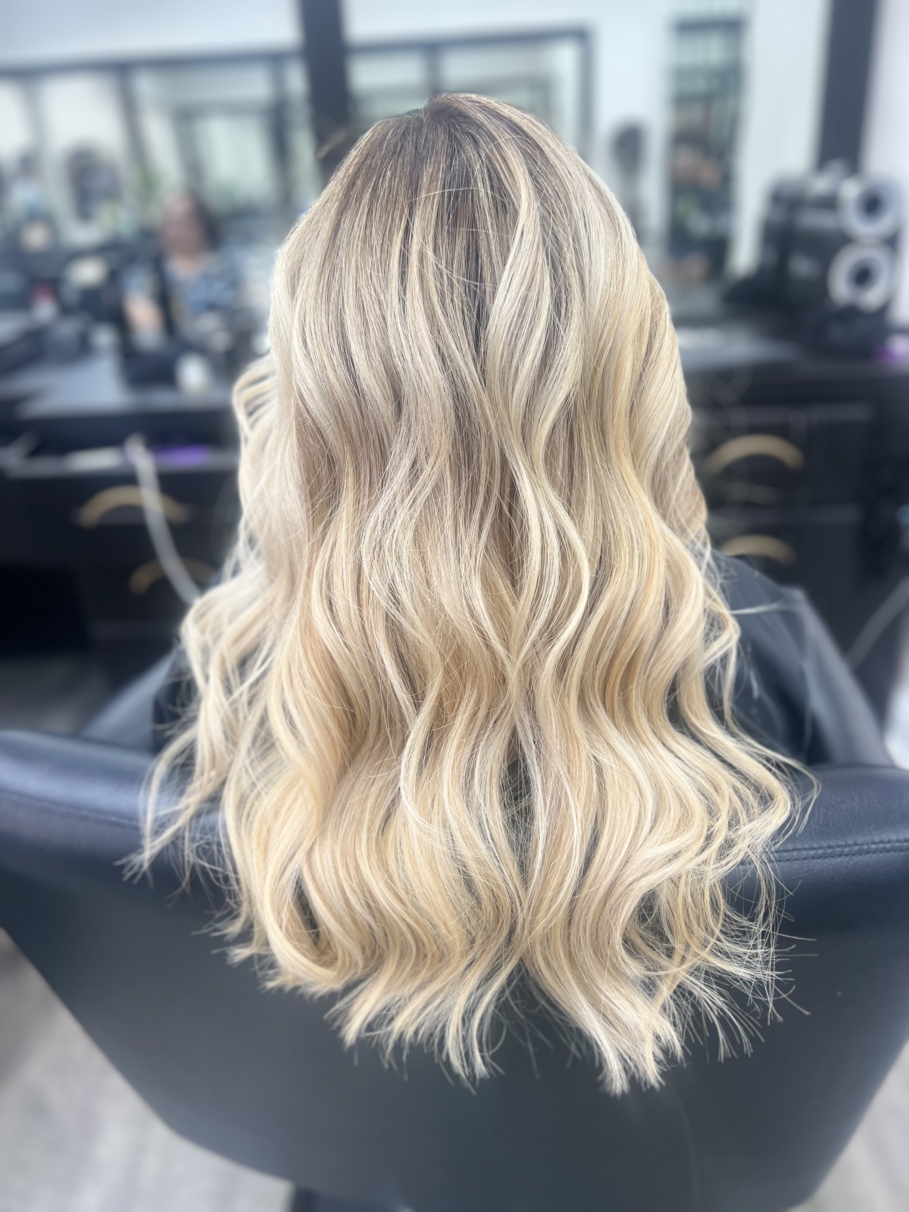 Stunning long wavy blonde balayage hair, back view inside the salon