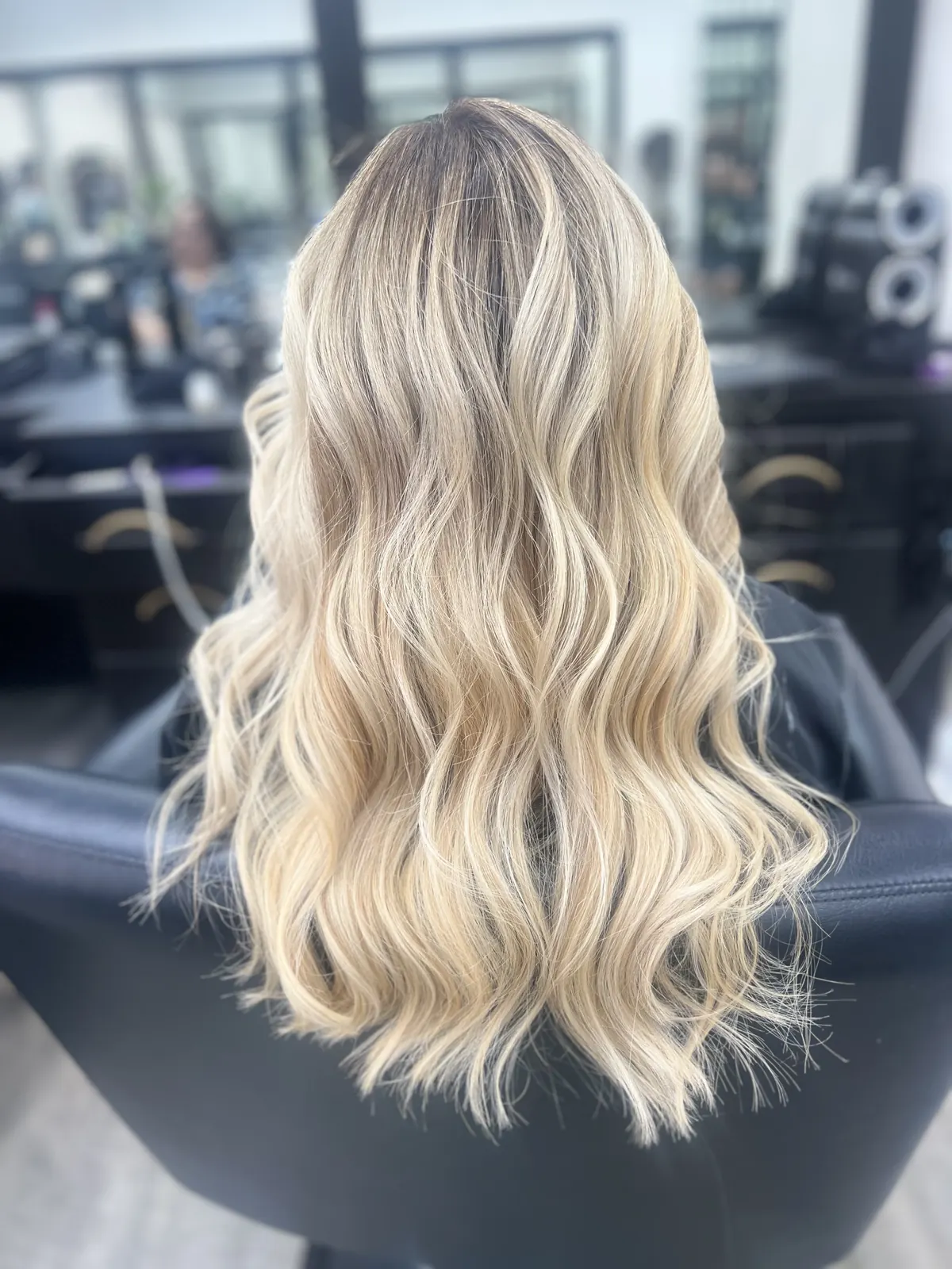 Stunning long wavy blonde balayage hair, back view inside the salon
