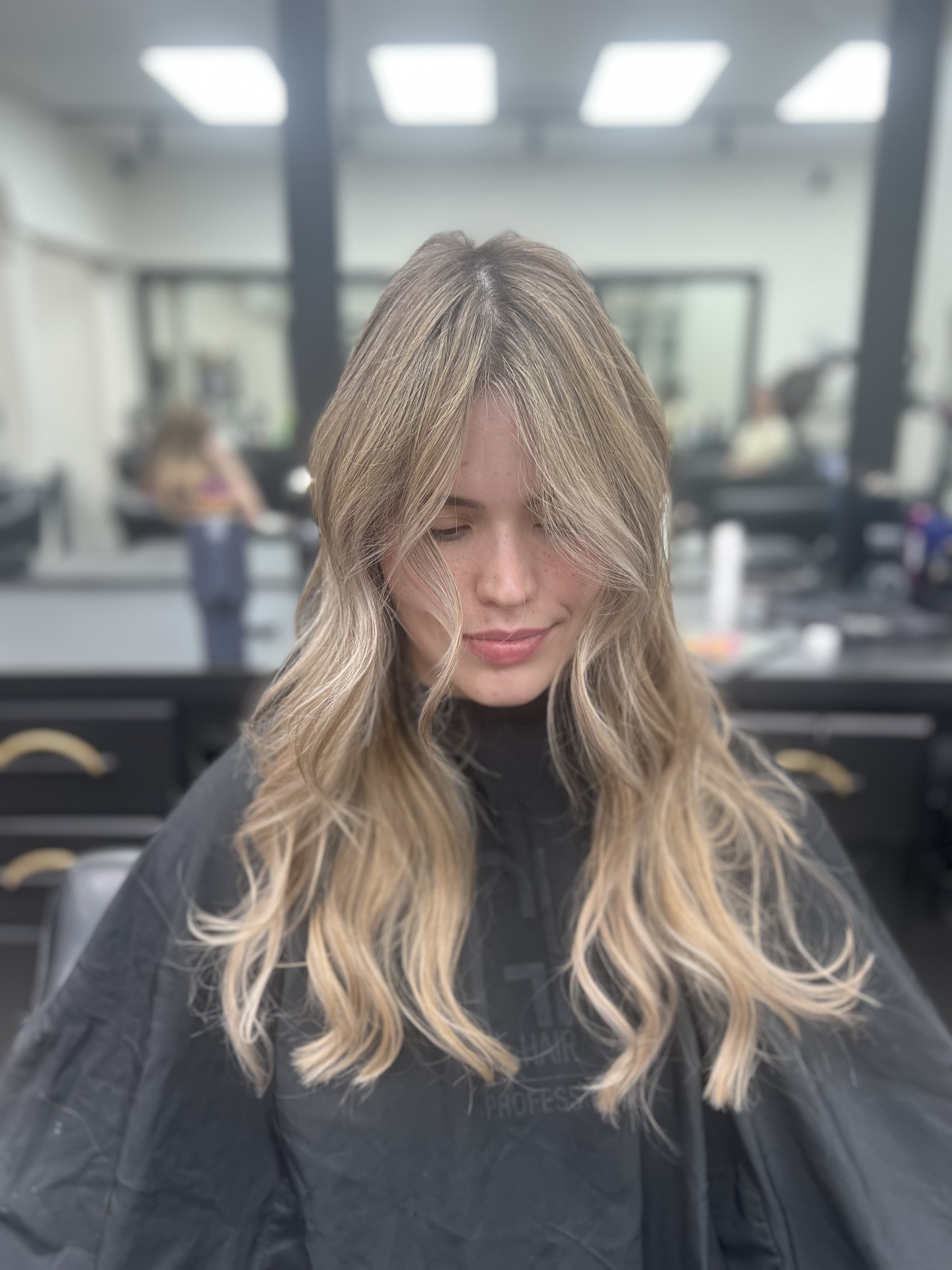 Long blonde balayage with curtain bangs, client inside the salon