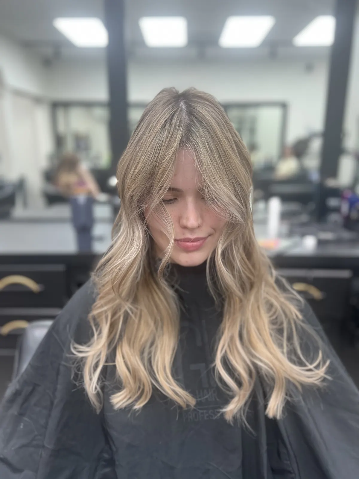 Long blonde balayage with curtain bangs, client inside the salon
